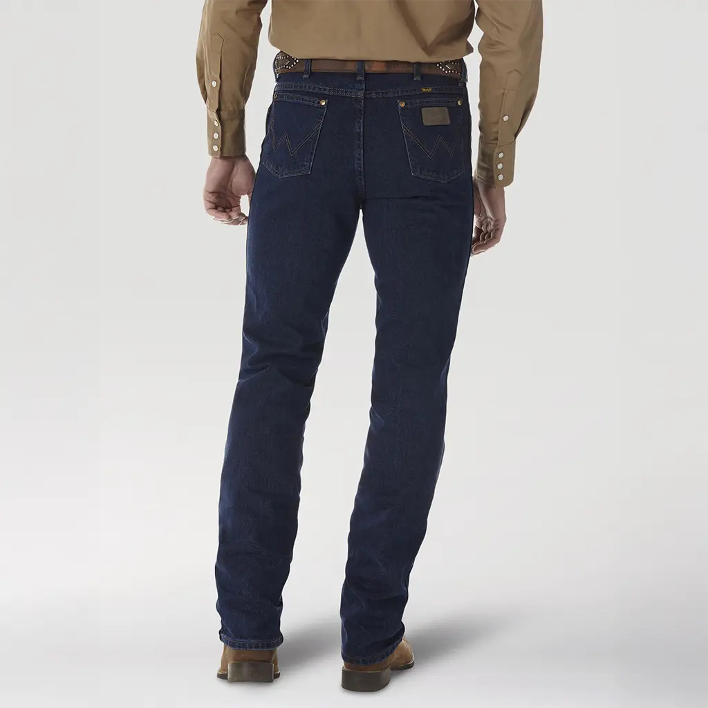 Back studio view of a model wearing Wrangler Men's 0936DSD Dark Stone Cowboy Cut Slim Fit jeans showing the high waist, trophy belt buckle, and dark indigo denim tone.