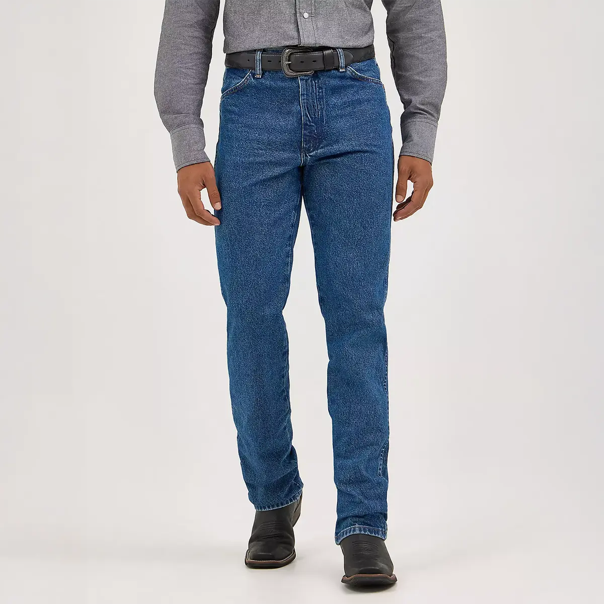 Front view of a model wearing Wrangler Men's Cowboy Cut Slim Fit stonewash blue jeans paired with a button-down shirt, black leather belt, and Western boots.