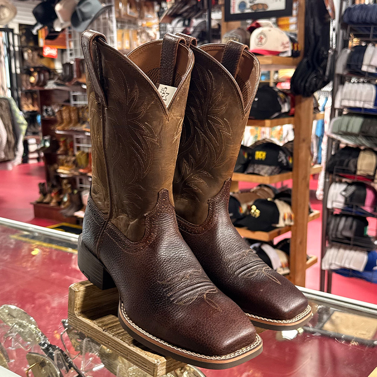 Pair of men's brown Ariat square toe cowboy boots on a glass display case in a western store.
