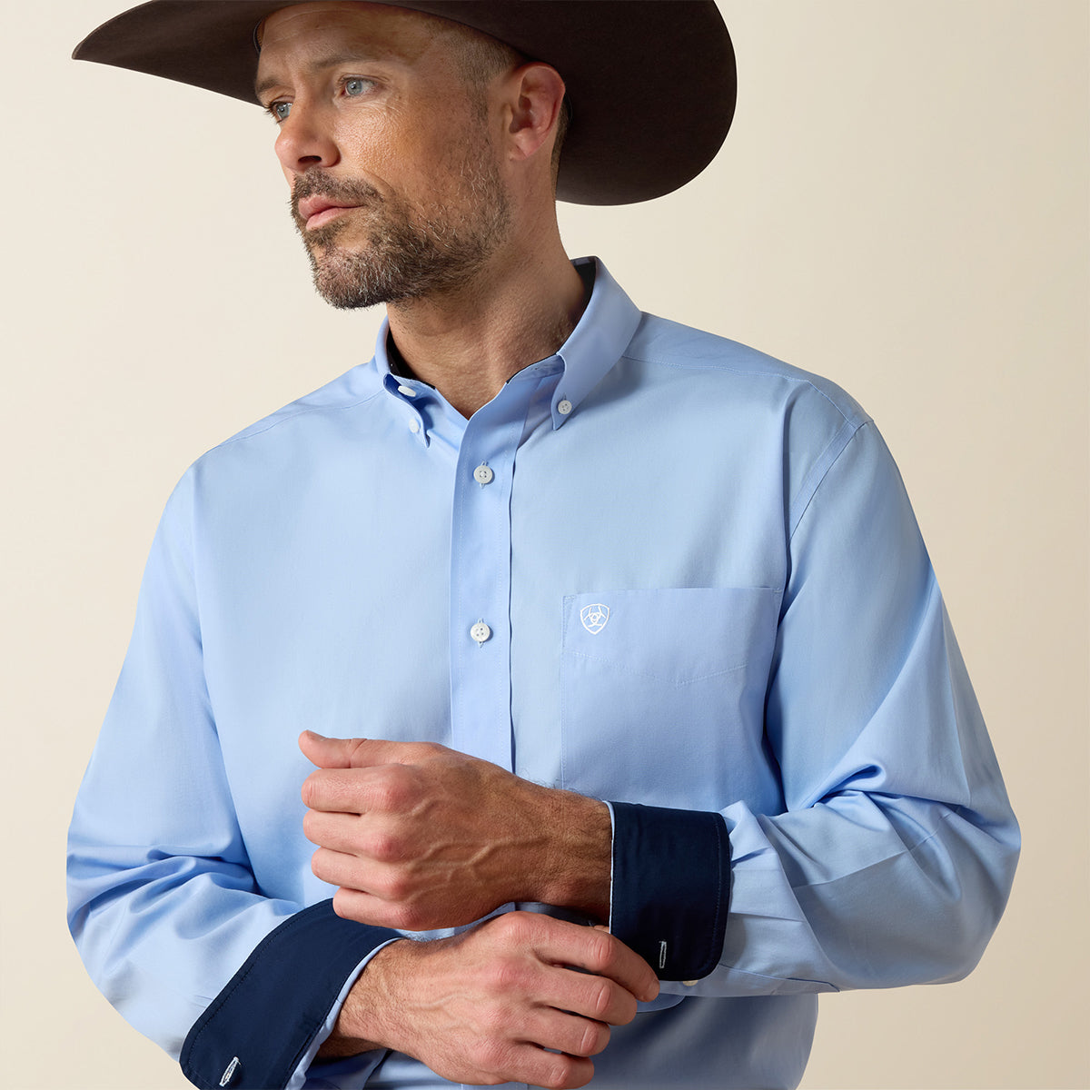 Man wearing a light blue shirt and brown cowboy hat against a beige background.