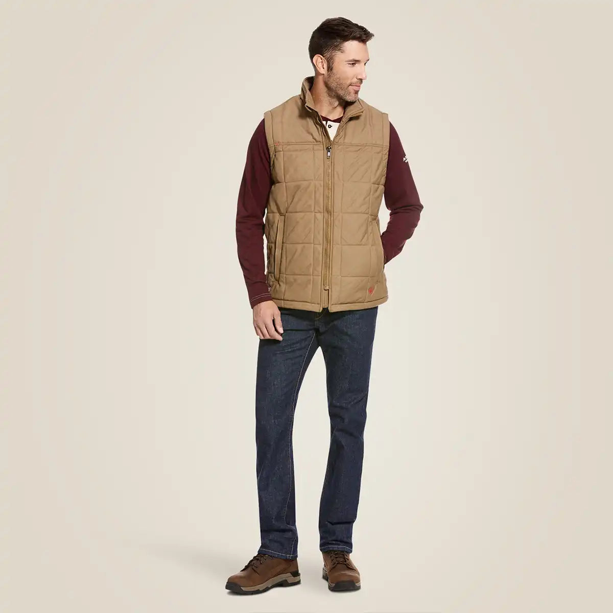 Front view of a man wearing the Ariat Men's Field Khaki FR Crius insulated quilted canvas vest over a long sleeve shirt.