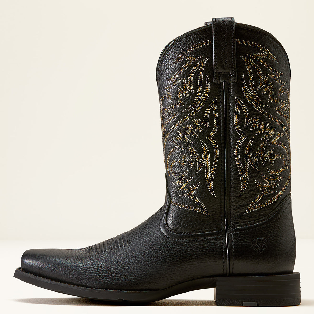 Ariat men's black cowboy boot with decorative tan stitching on the shaft, shown in a side profile against a light beige background.