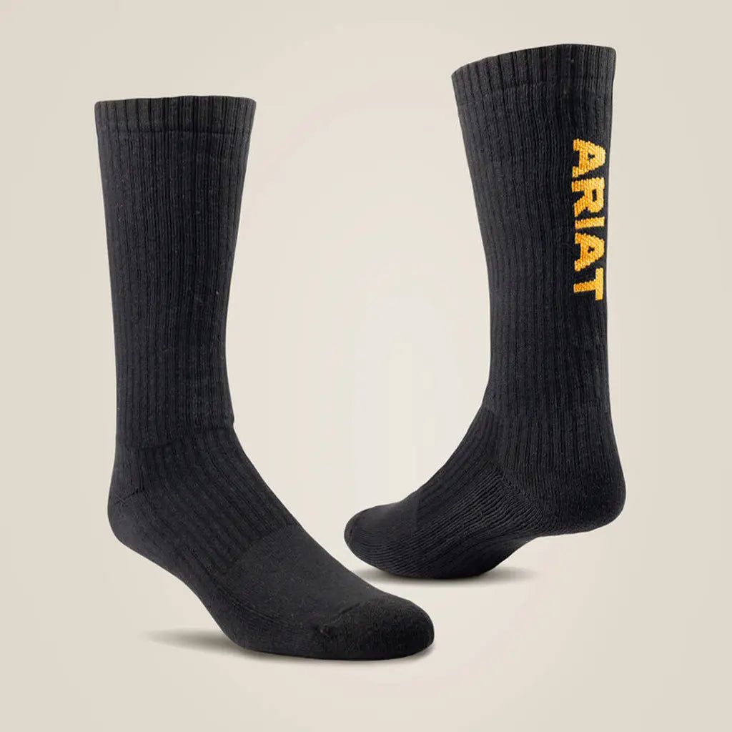 A pair of black crew-length boot socks displayed against a light beige background, featuring ribbed uppers and yellow vertical "ARIAT" text printed along the side of the leg.