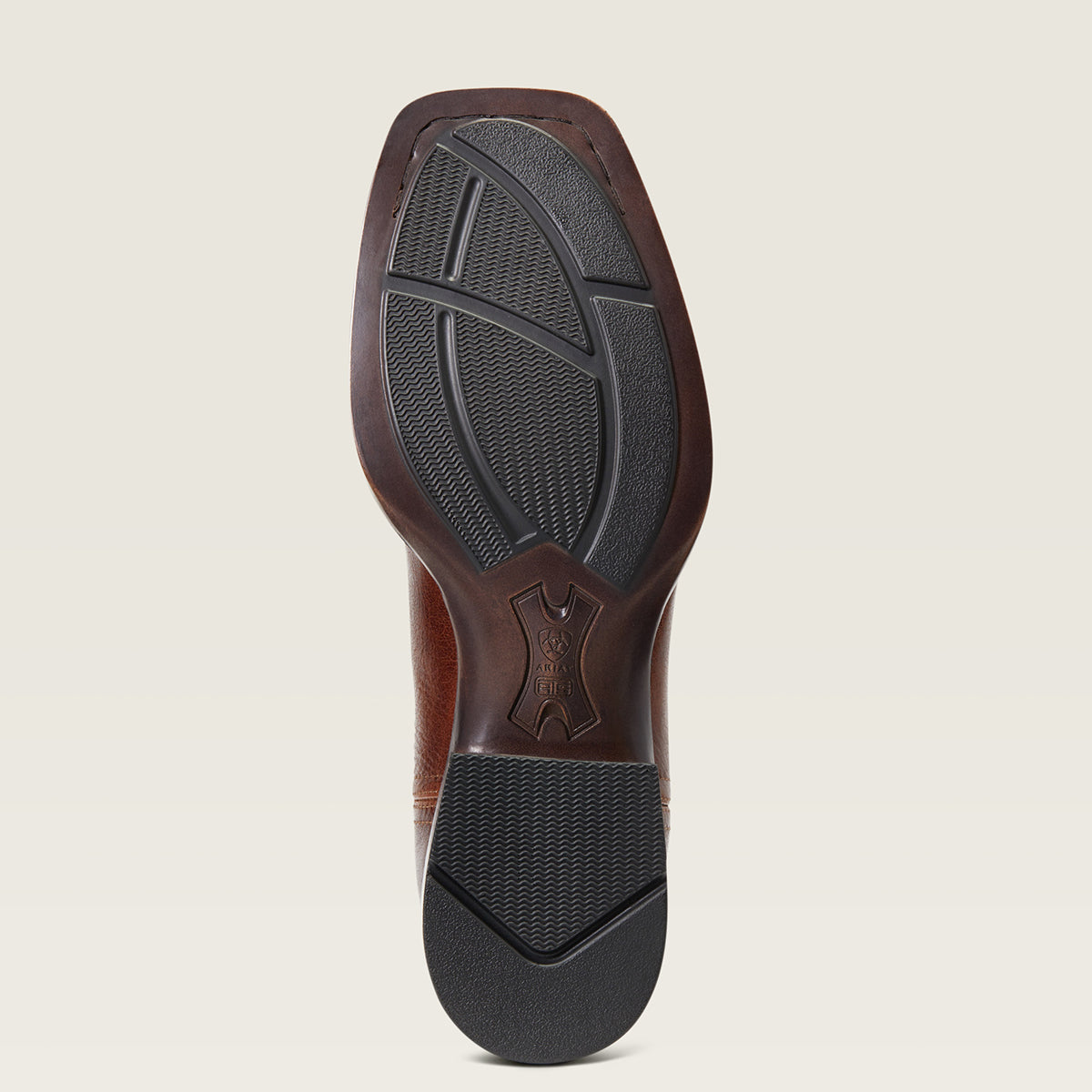 A top-down view of a brown leather Ariat sole, showing the textured black outsole and a debossed logo in the center, set against a solid light beige background.