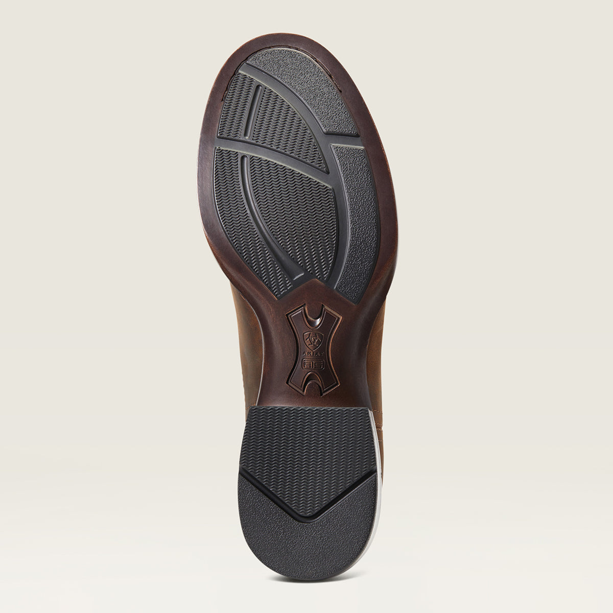 A close-up shot of the Ariat outsole of a brown leather boot, showing the tread pattern and a debossed logo on the heel, set against a light beige background.