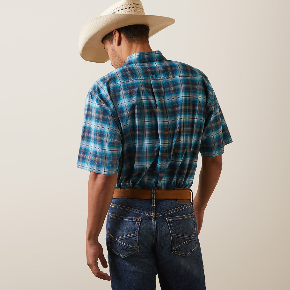 Back view of a man wearing the Ariat Men's Pro Kenneth blue and teal plaid short sleeve button-down shirt with straw cowboy hat and jeans.