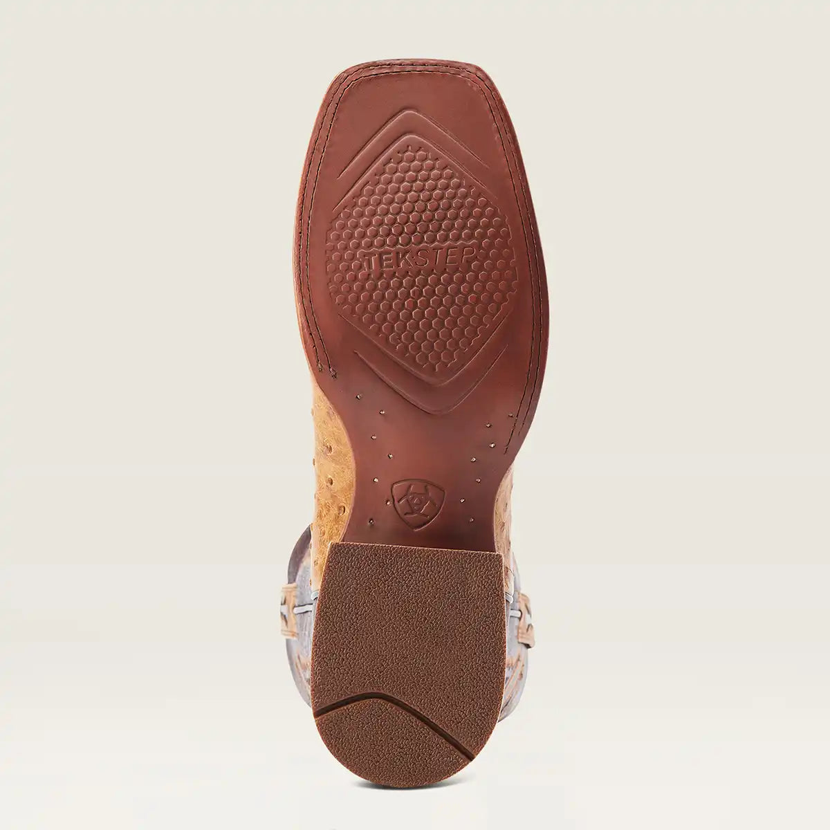 A close-up bottom view of a western boot showing the sole, with a brown rubber outsole, textured brown tread, and a tan and silver patterned leather upper.