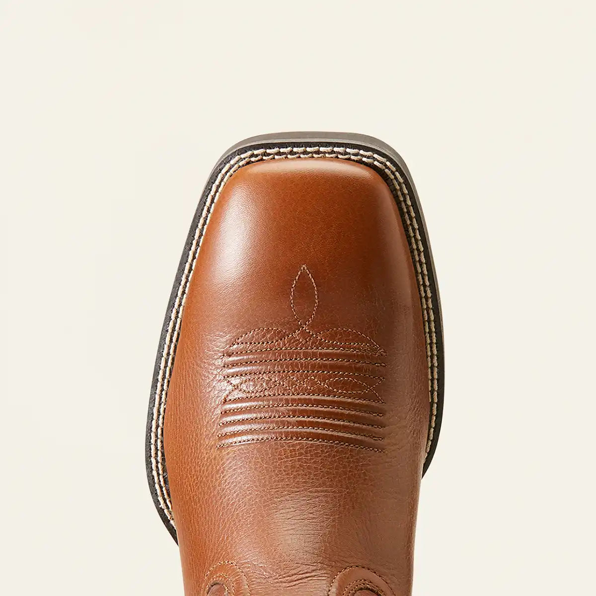 A close-up top-down view of a brown leather boot toe, showing a Ariat square toe with decorative stitching and a dark sole edge, set against a plain off-white background.