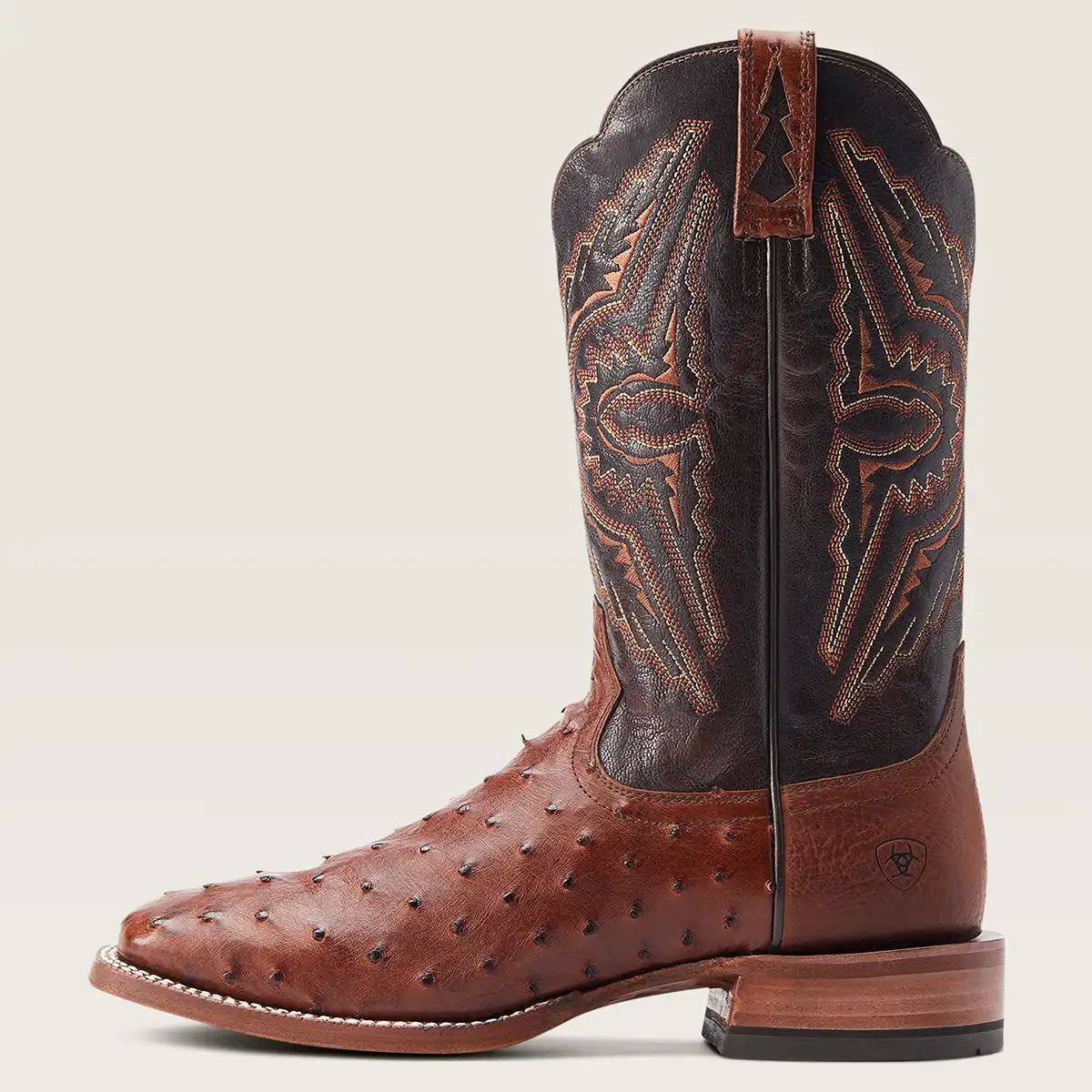 A single brown leather Ariat cowboy boot with an ostrich leather toe and dark brown shaft featuring intricate western stitching, shown against a light beige background.