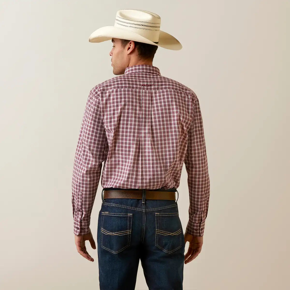 A man shown from the back wearing a red and white plaid long-sleeve western shirt, dark blue jeans, a brown belt, and a cream-colored cowboy hat against a plain beige background.