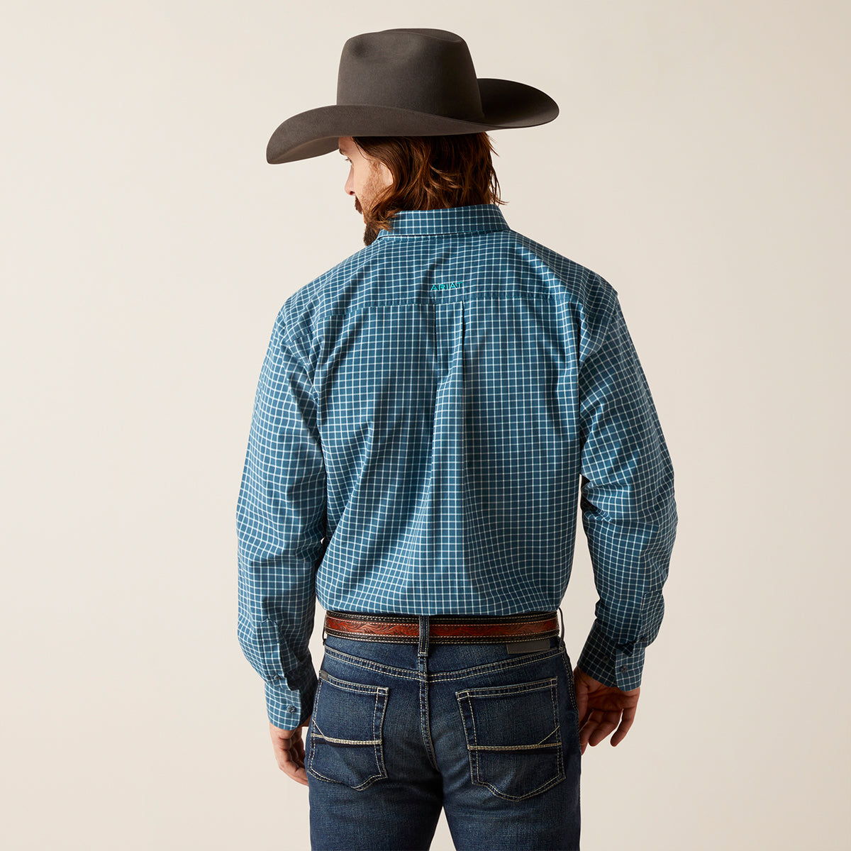 A man wearing a blue and white checkered western long-sleeve Ariat shirt, blue jeans, and a dark brown cowboy hat, shown from the back against a light beige background.