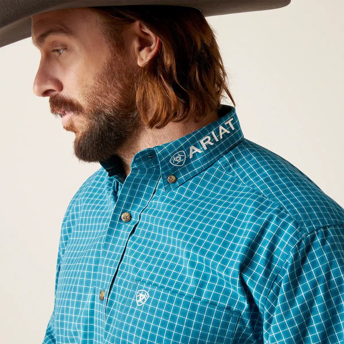 Man wearing a blue checkered shirt with Ariat logo on a white background.