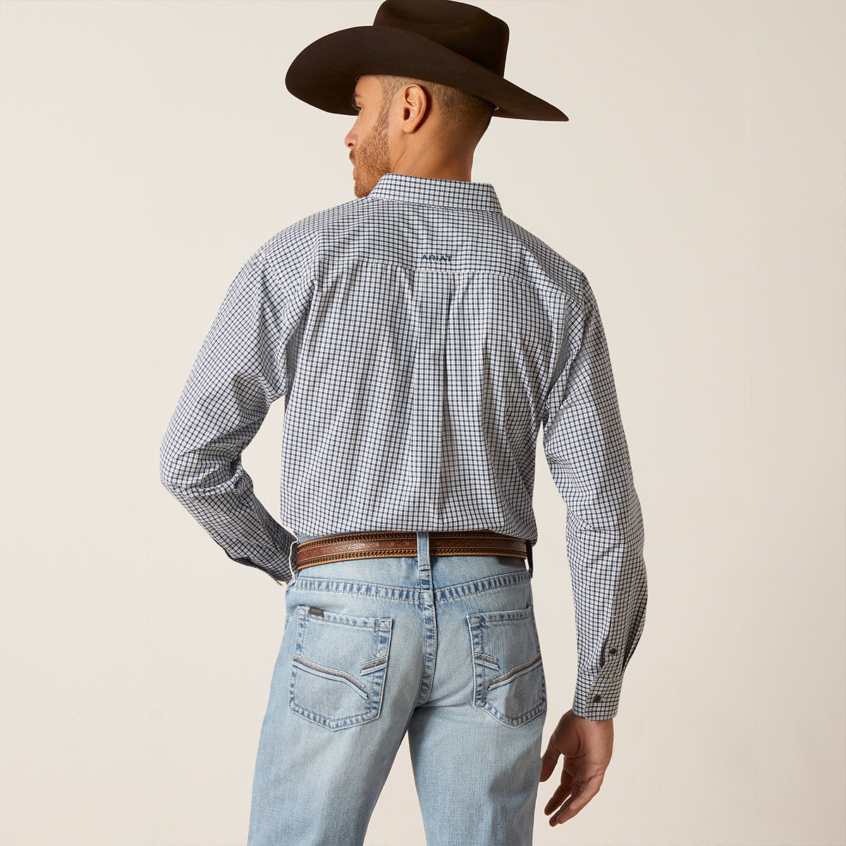 A man shown from the back wearing a brown cowboy hat, a blue and white gingham long-sleeve western shirt, and light blue jeans against a plain beige studio background.