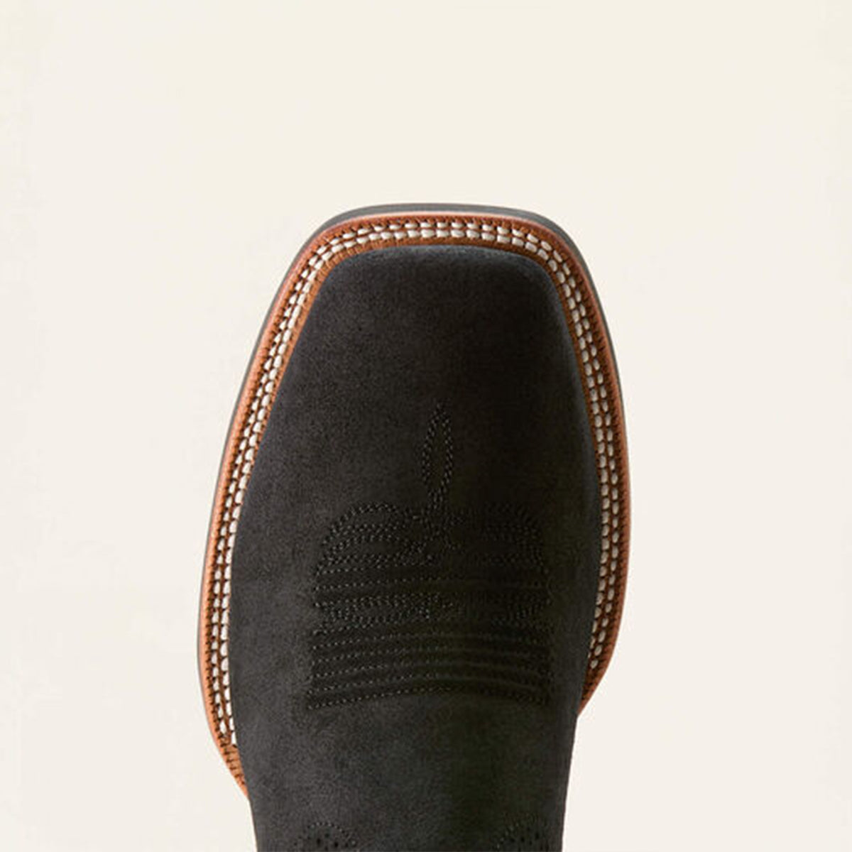 Close-up of a black suede square toe boot with brown stitching on a beige background.