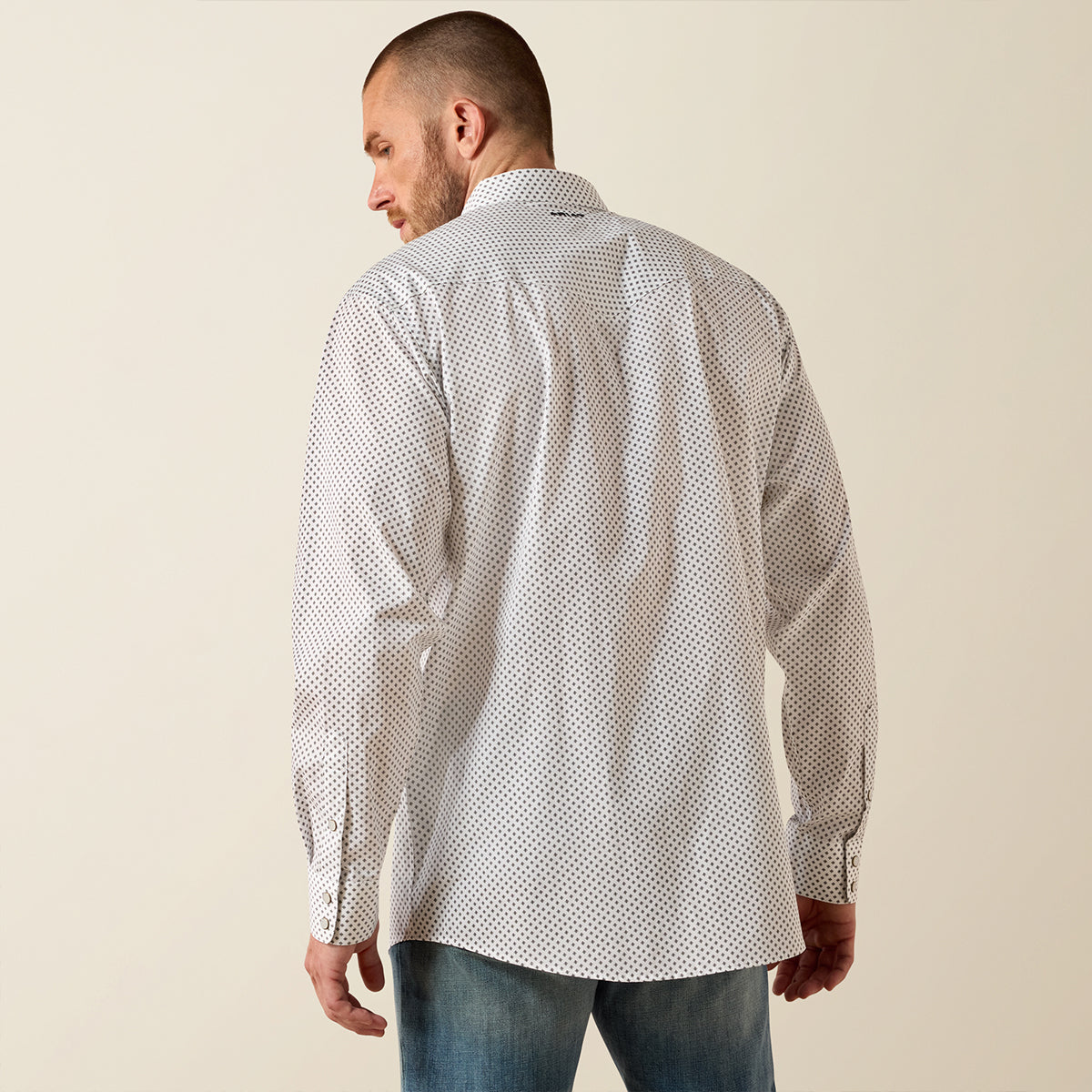 A man wearing a white long-sleeve button-down shirt with a small black geometric pattern, shown from the back against a plain beige background.