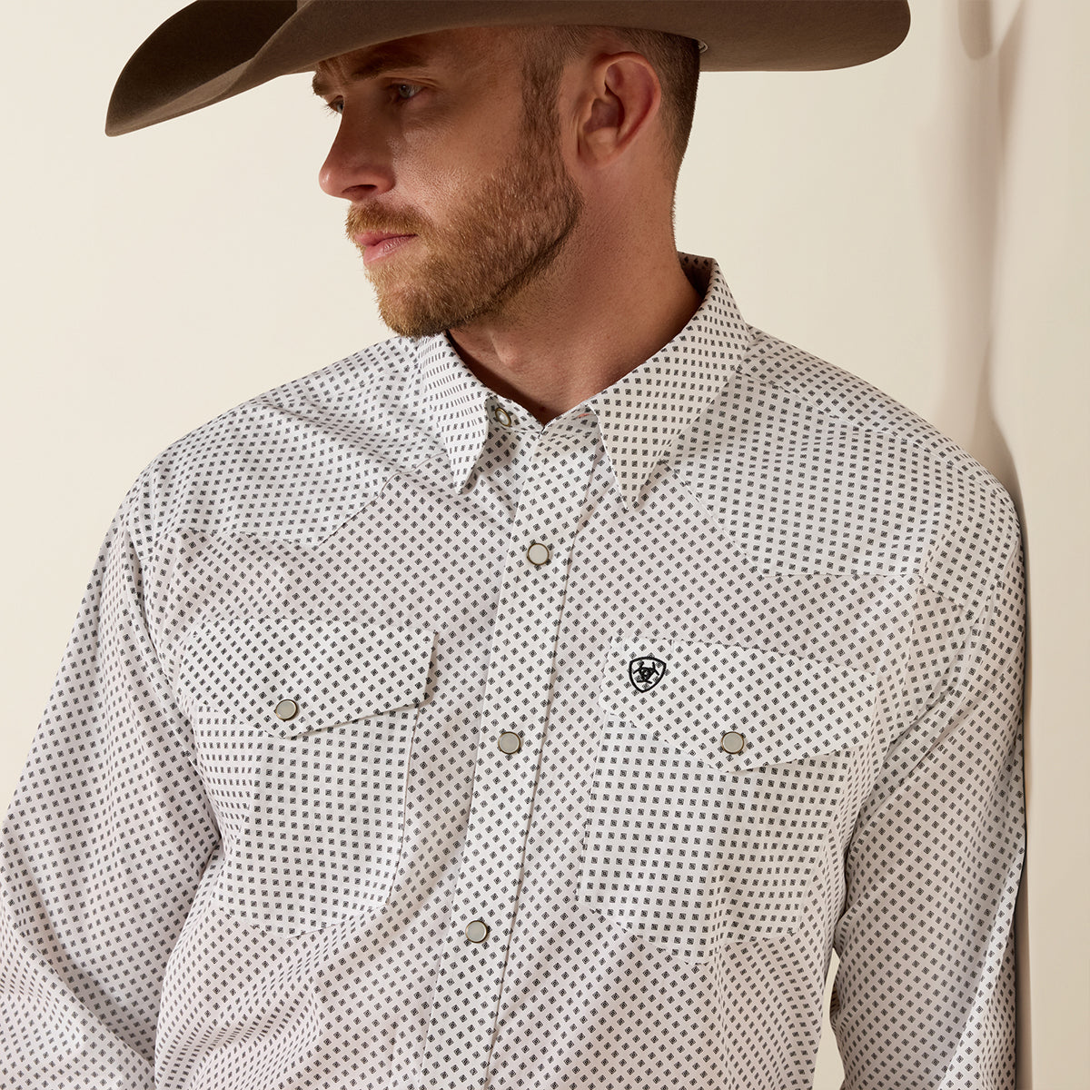 Man wearing a patterned shirt and cowboy hat against a beige background.
