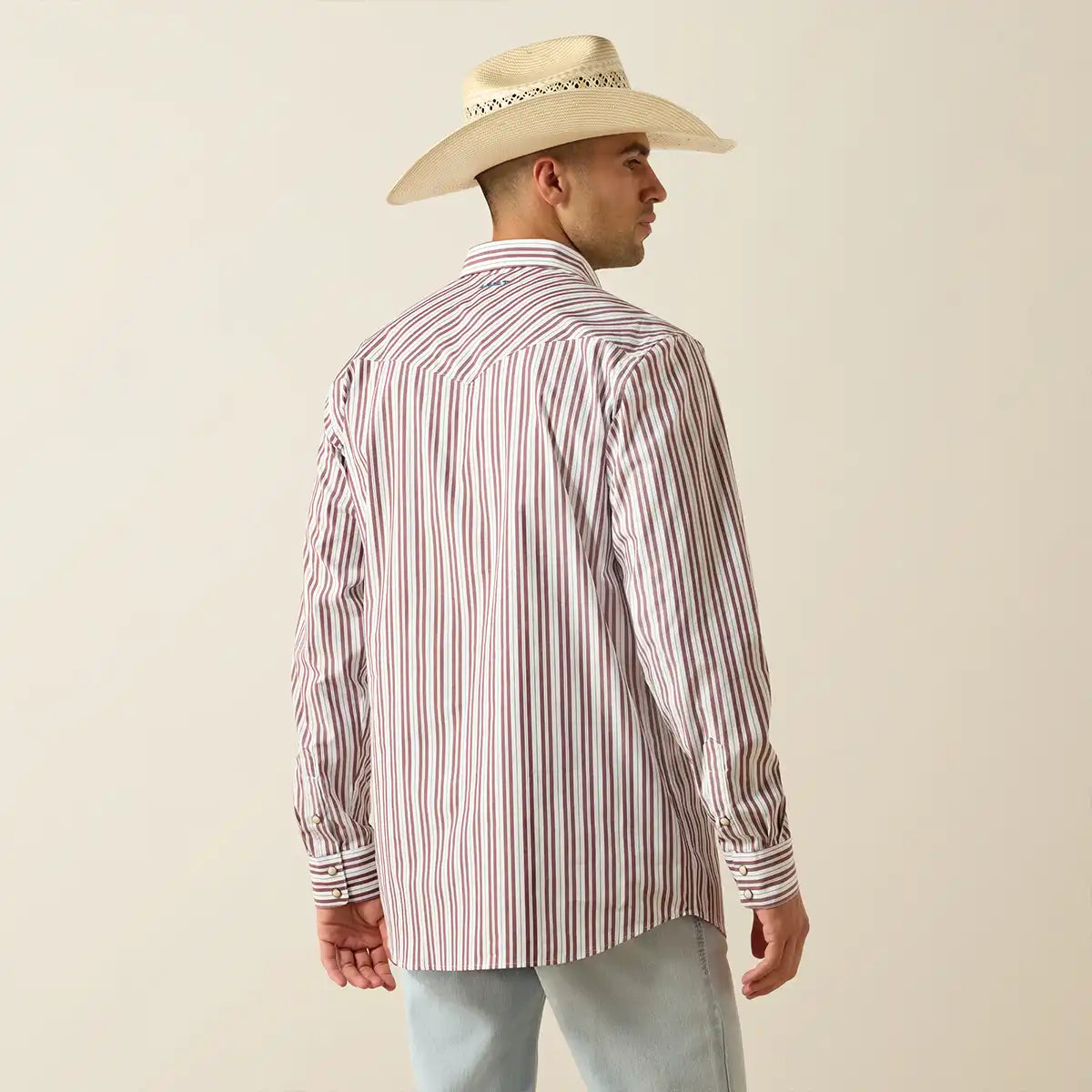 Man wearing a striped Ariat shirt and cowboy hat on a beige background.