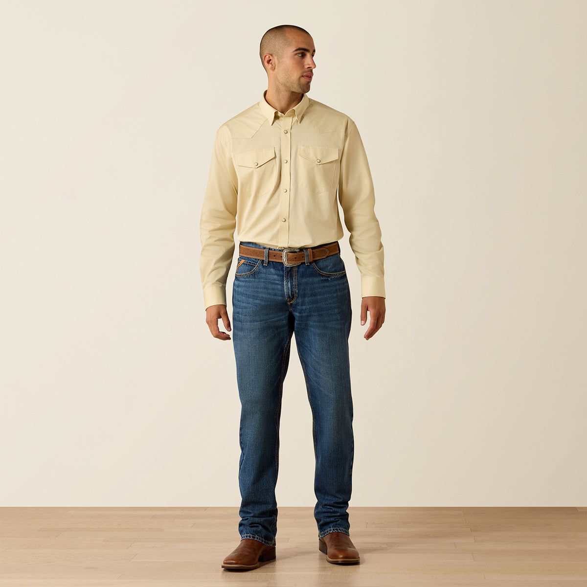 Front view of a man wearing the Ariat Men's Creme Brulee light tan long sleeve Western snap shirt with snap flap pockets.