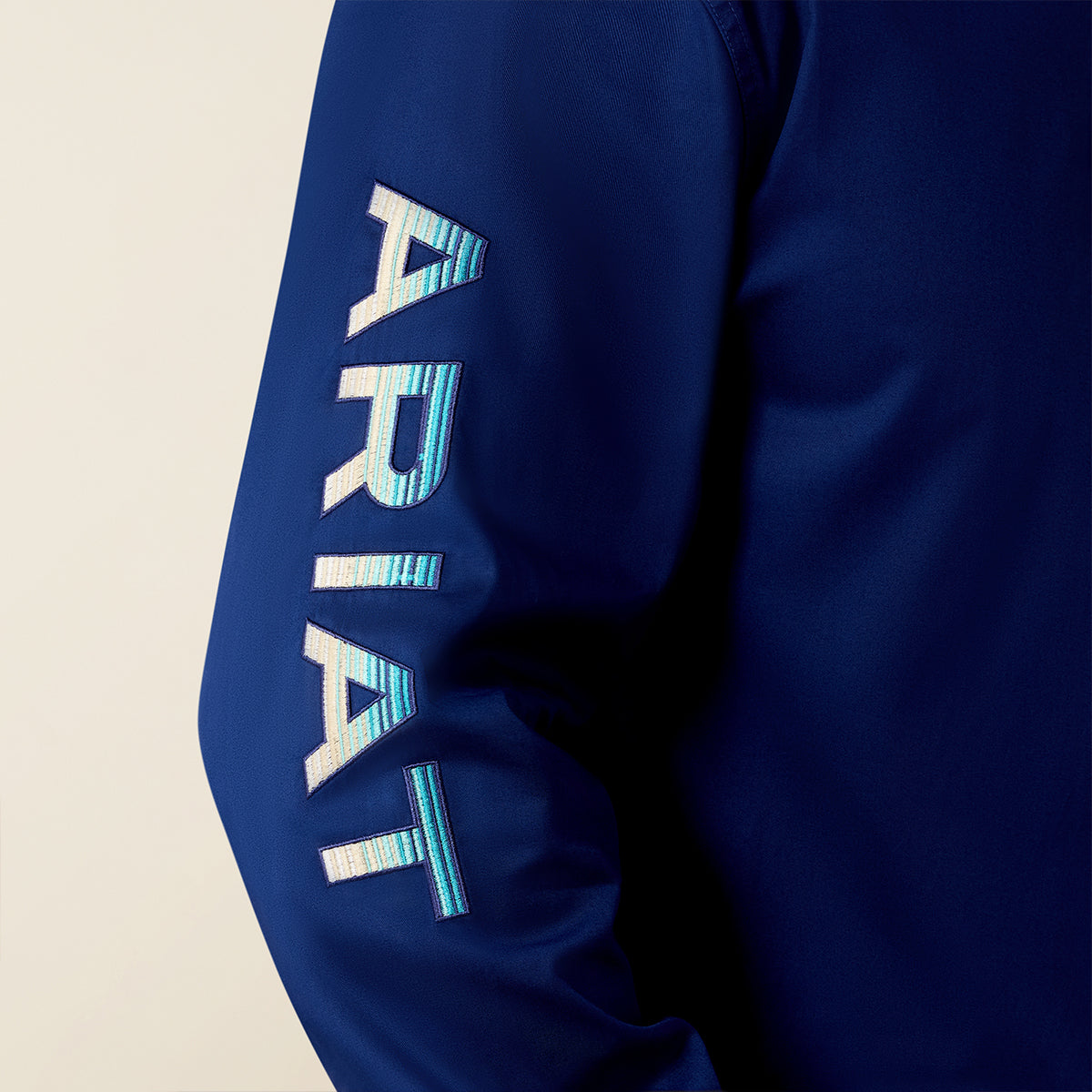Blue sleeve with 'ARIAT' embroidery on a beige background.