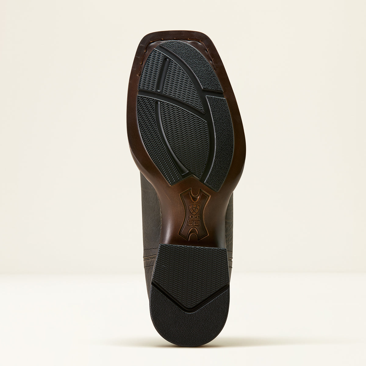 The outsole of a Ariat leather cowboy boot with a black treaded rubber sole, shown from a top-down view against a light beige background.