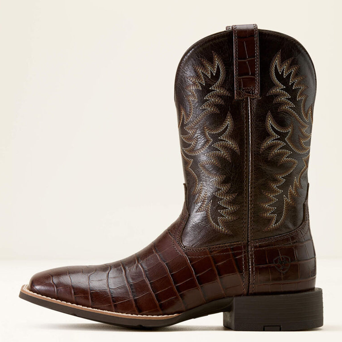 Side profile of Ariat brown croc print cowboy boot with intricate embossing on a beige background.