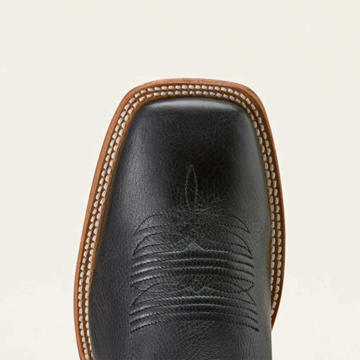 Close-up of a Ariat Country Road black leather square toe boot with brown stitching on a beige background.