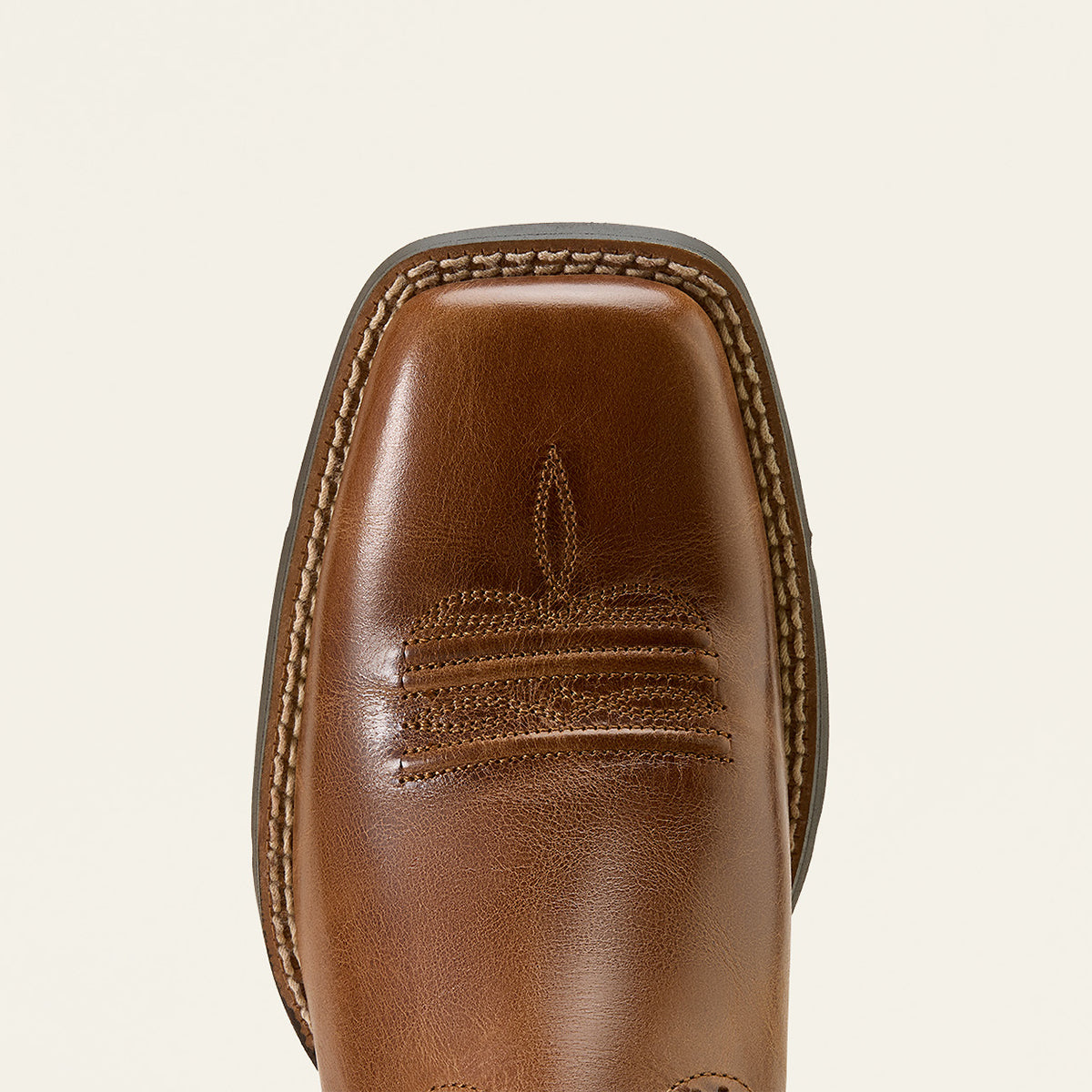 Close-up of the Ariat bermuda square toe of a brown leather boot with decorative stitching and a square toe, shown on a light cream background.