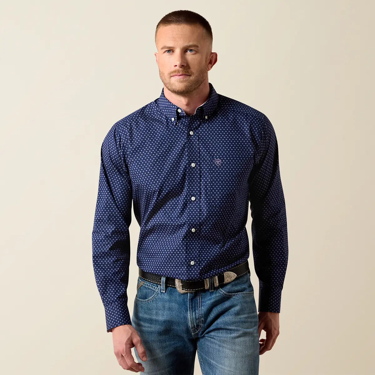 Front studio view of the male model wearing the Ariat dark navy geo print shirt tucked into light wash denim jeans with a Western belt.