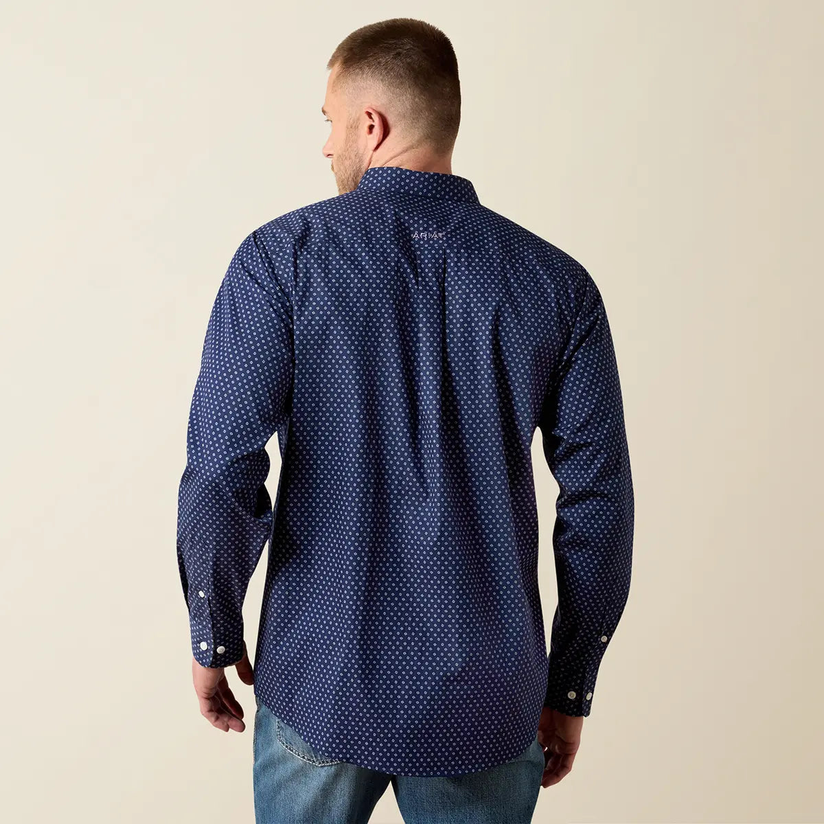 Rear studio view of a male model wearing the Ariat men's dark navy geo print long sleeve shirt displaying the small Ariat logo embroidered on the back yoke.