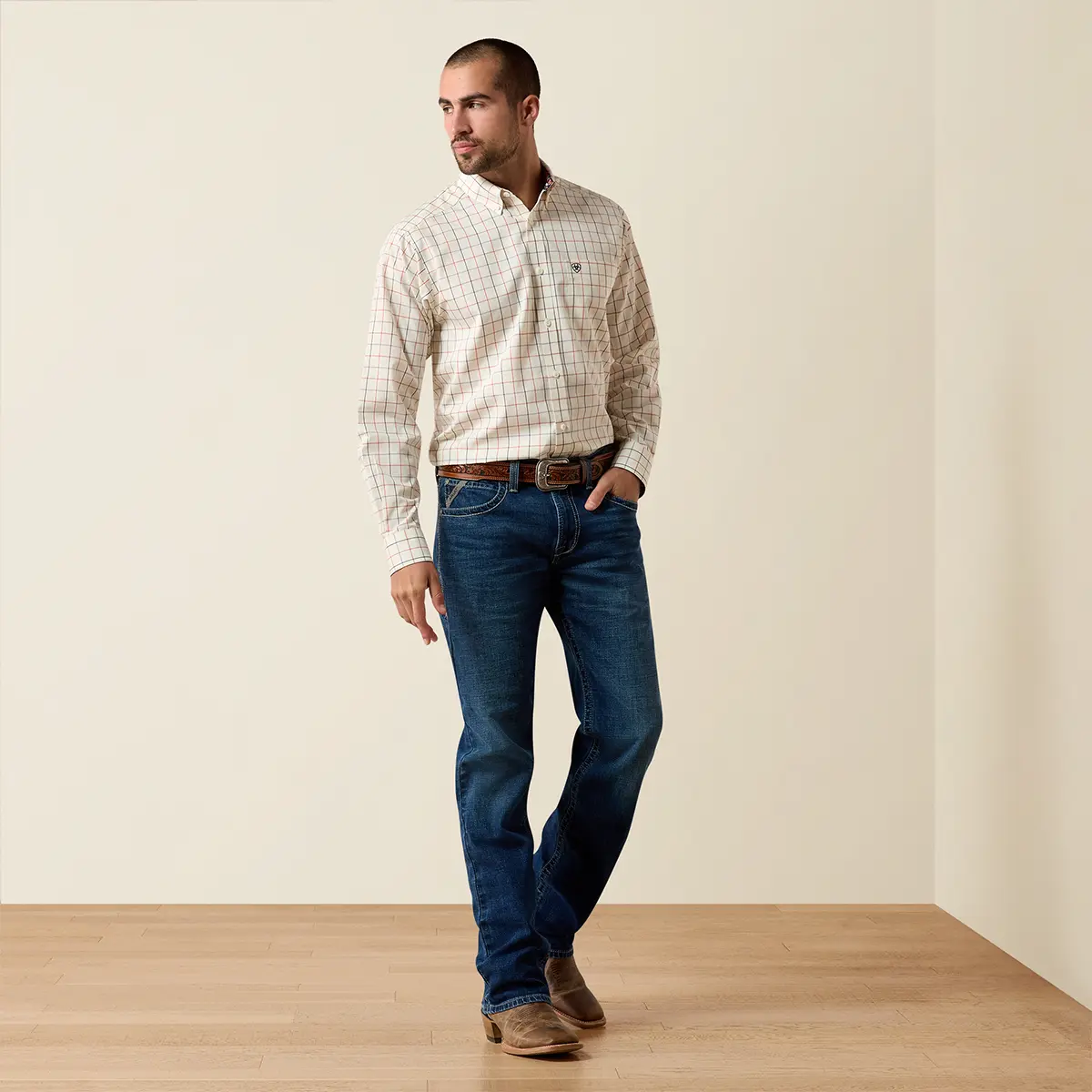 Full-body studio lifestyle view of the male model wearing the Ariat Arctic Wolf plaid shirt, blue jeans, and brown leather cowboy boots.