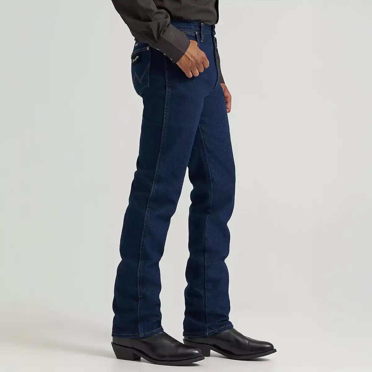 Side profile view of a man wearing Wrangler Men's Cowboy Cut Silver Edition dark denim jeans over black Western boots.