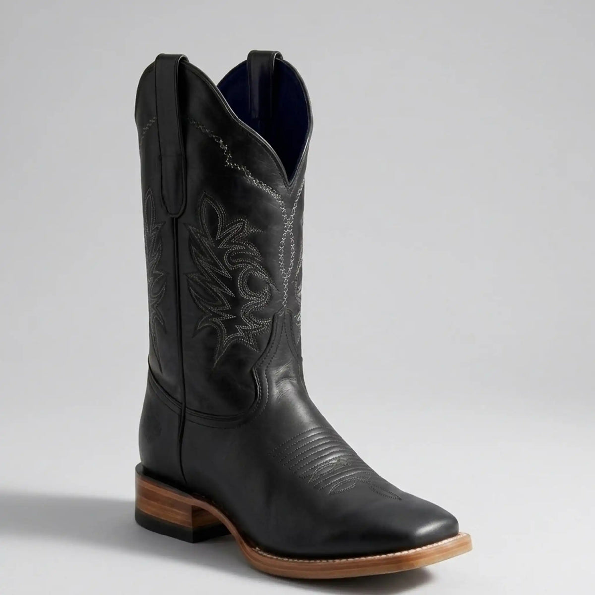A single black leather cowboy boot with decorative western stitching, a square toe, and a stacked wood-look heel, photographed on a light gray studio background.