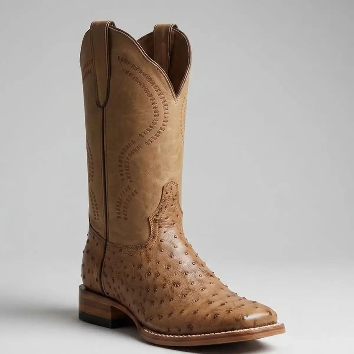 A single tan cowboy boot with a smooth shaft and an ostrich-textured leather foot, shown from a three-quarters angle against a light gray background.