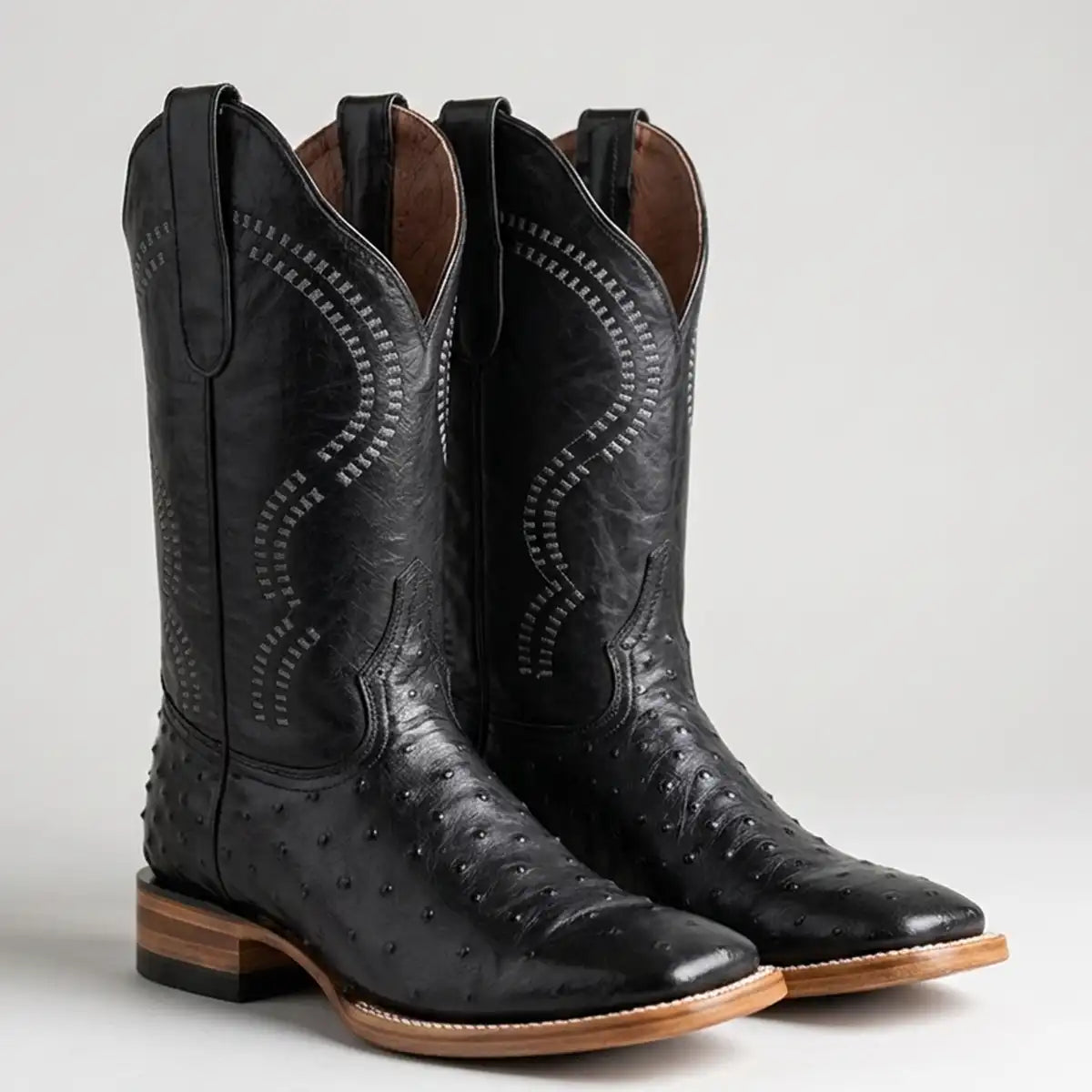 A pair of black western boots with ostrich-embossed leather detailing and decorative stitching, shown on a light gray background.