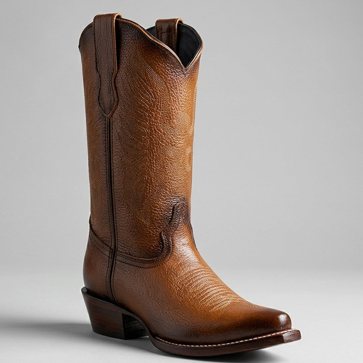 Women's light brown leather cowboy boot with a textured grain finish, a pointed toe, and a low stacked heel, photographed on a neutral light gray background.