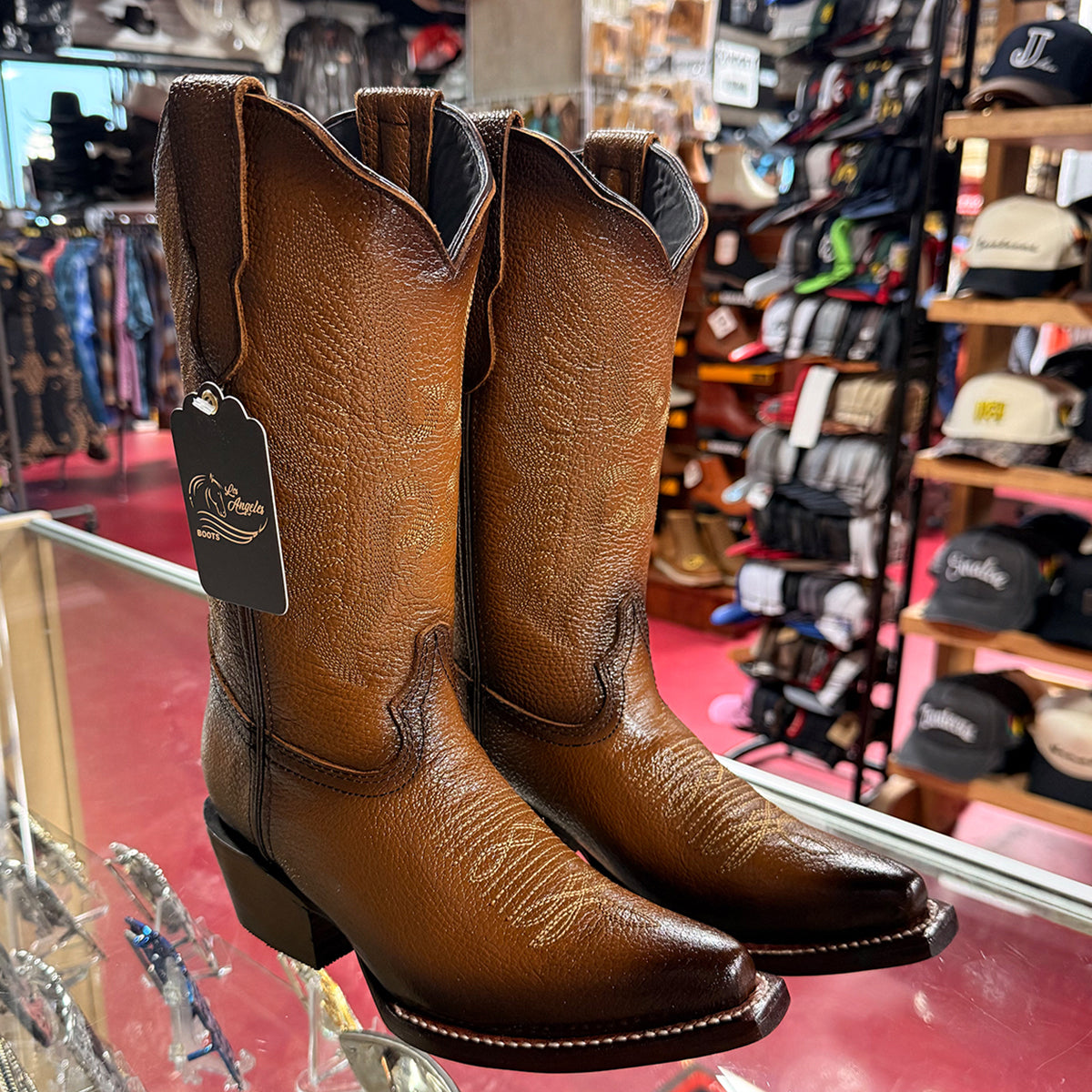Women's light brown leather cowgirl boots with a textured grain finish, displayed on a glass counter inside a western store.