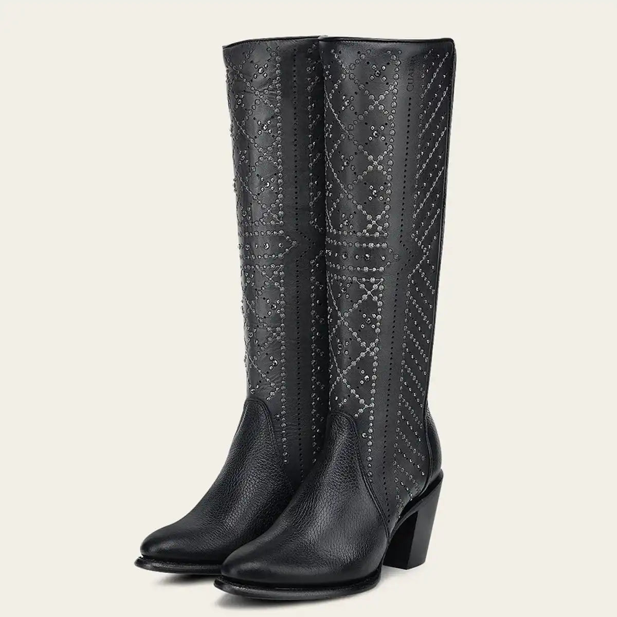 A pair of Cuadra women's black leather knee-high boots with a textured grain finish, featuring geometric diamond studded patterns on the shafts and a low block heel, shown against a solid light beige background.
