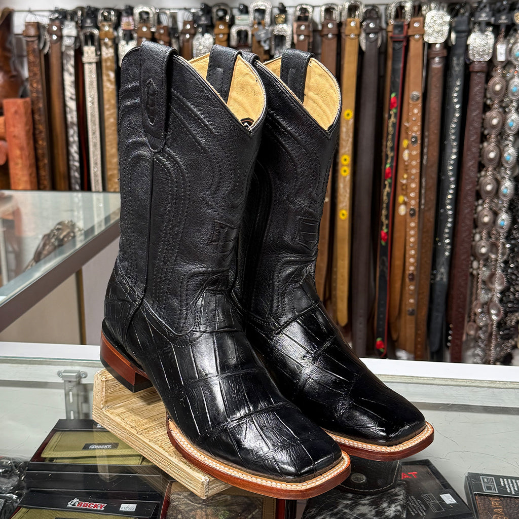 Retail counter display view of the Los Altos black alligator square toe boots sitting on a glass display inside a Western boot store.
