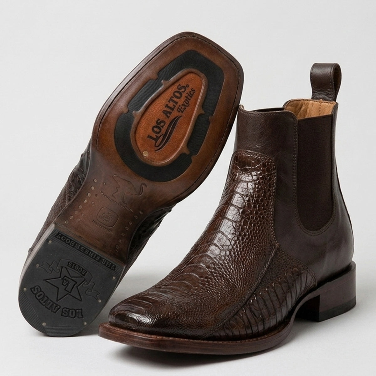 A pair of Los Altos men's dark brown ostrich leg leather western boots with elastic side panels, shown on a light gray background. One boot is standing upright while the other is turned to show the sole, which features the brand name 'Los Altos Exotics'.