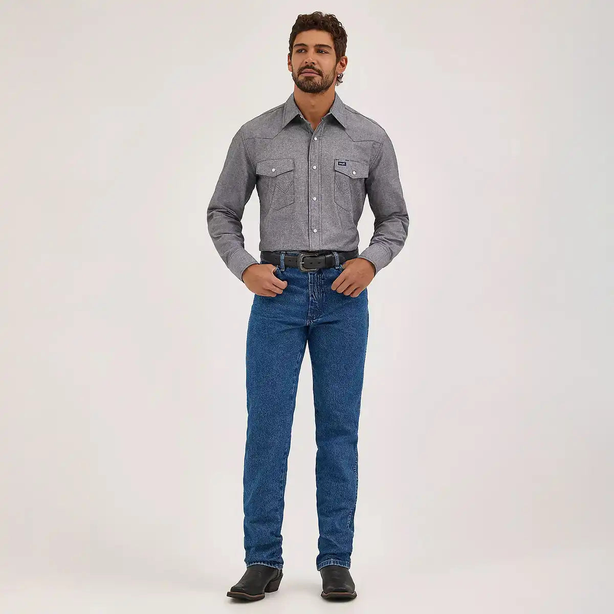 Full length front view of a man wearing Wrangler Men's Cowboy Cut slim fit stonewashed jeans with grey Western shirt and black boots.
