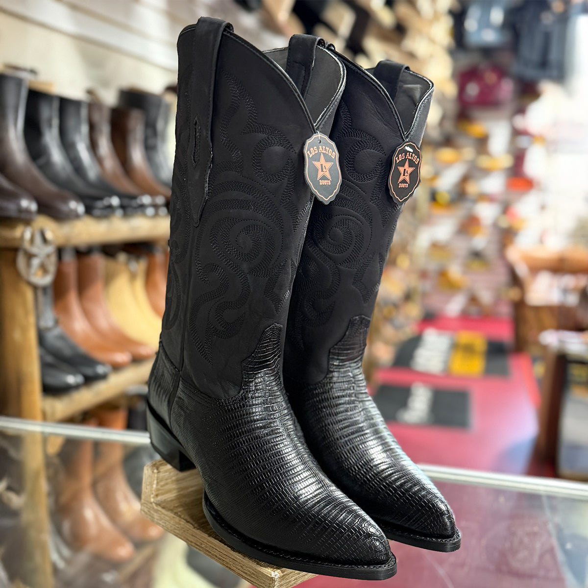 A pair of Los Altos black lizard western cowboy boots j-toe, displayed on a wooden stand inside a western store.