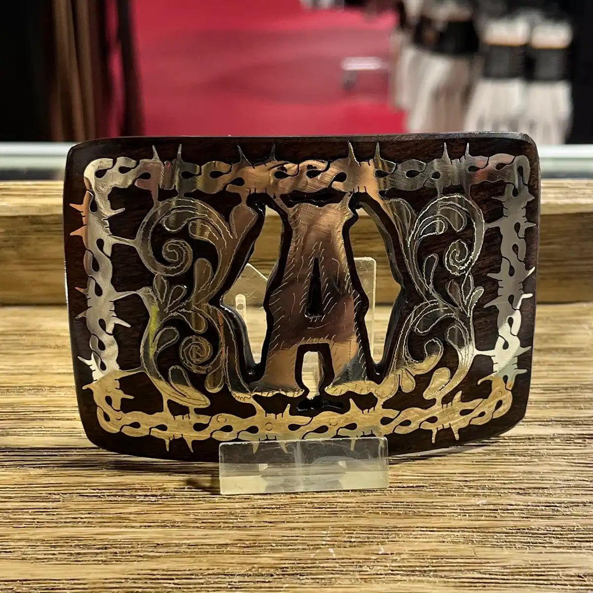 In-store counter display view of the handcrafted mesquite wood belt buckle showing the Monogram A inlay on an acrylic stand.