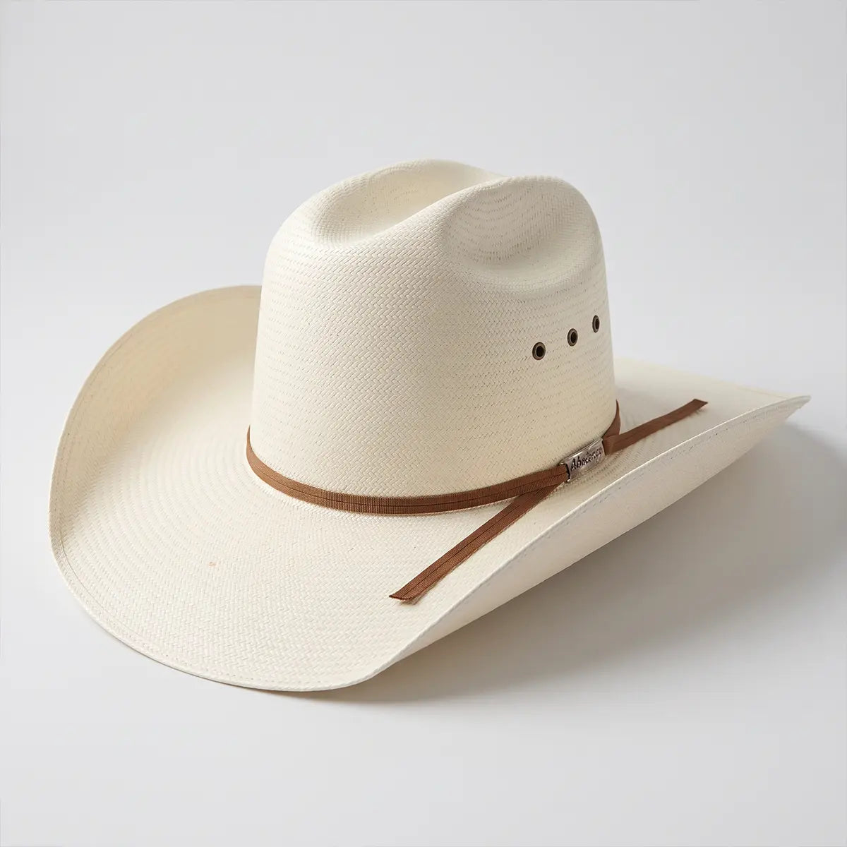 Studio three-quarter view of the Abolengo 30X natural Shantung straw Minnick cowboy hat on a white background highlighting the side eyelet vents and brown ribbon hatband.