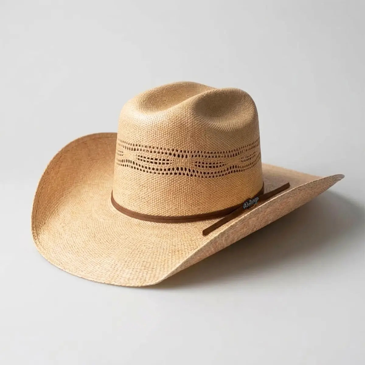 Three-quarter studio profile view of an natural tan straw cowboy hat featuring a vented Cattleman crown, brown ribbon hatband with script logo clip, and curved brim.