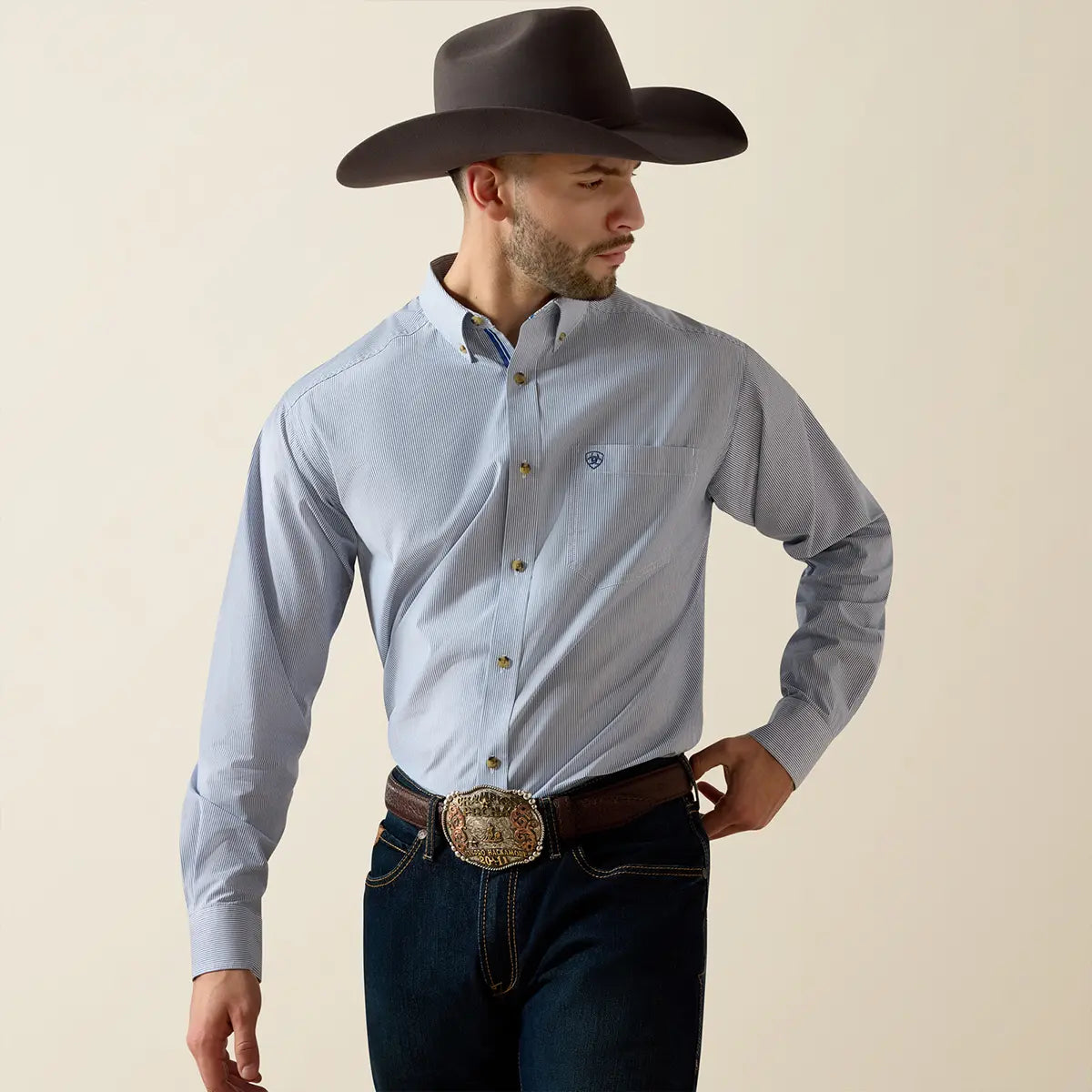 Front medium shot of the model wearing the Ariat Dayne True Blue striped shirt tucked into dark denim with a western trophy buckle belt.