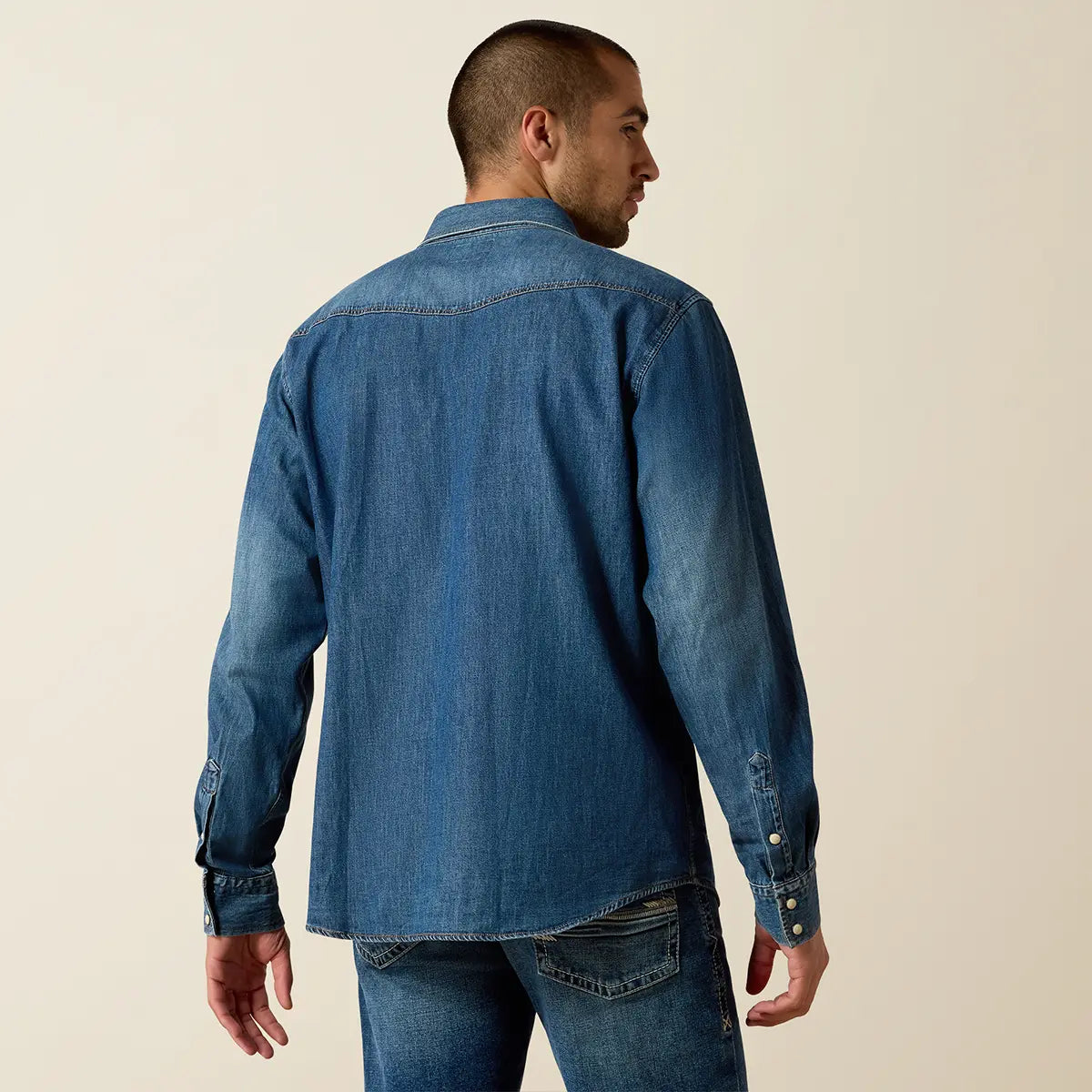 Rear view of the model showing the back fit and Western pointed back yoke of the Ariat Stone Blue denim shirt.