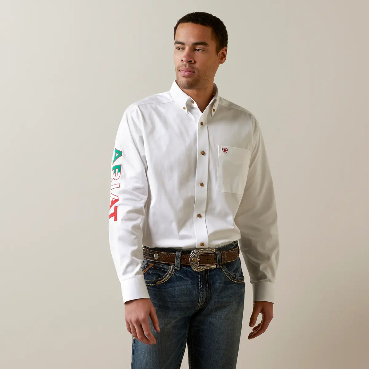 Front medium shot of the model wearing the Ariat white button-down shirt highlighting the chest pocket logo and green, white, and red sleeve embroidery.