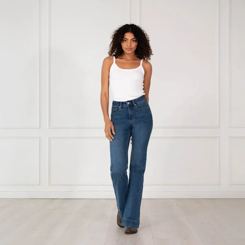 Full-length front view of a model wearing Rock & Roll Denim Women's Sculpted medium high rise trouser jeans with a white tank top.