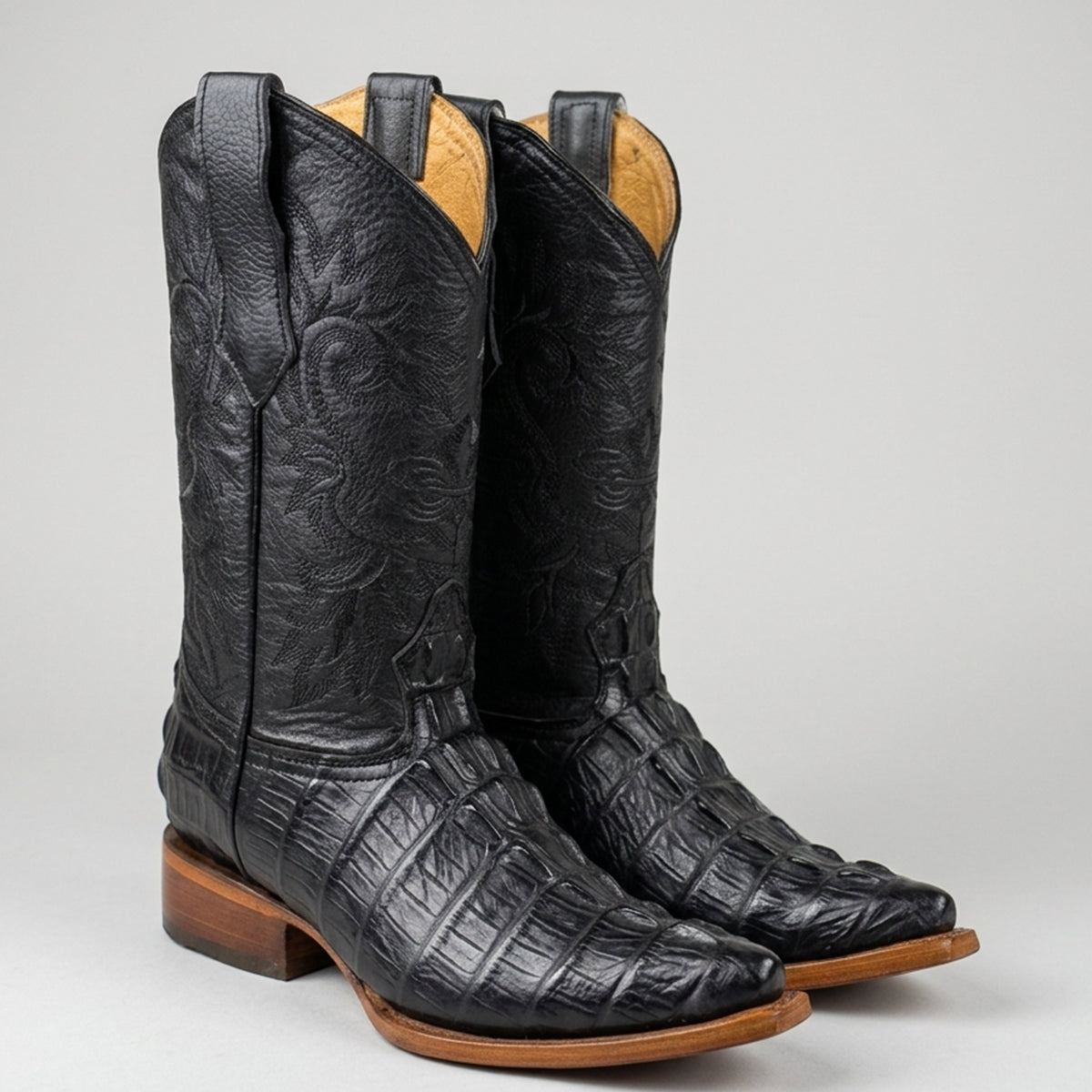 Pair of black crocodile tail print cowboy boots featuring a 2X pointy toe profile, 12-inch stitched leather shaft, and natural leather sole.