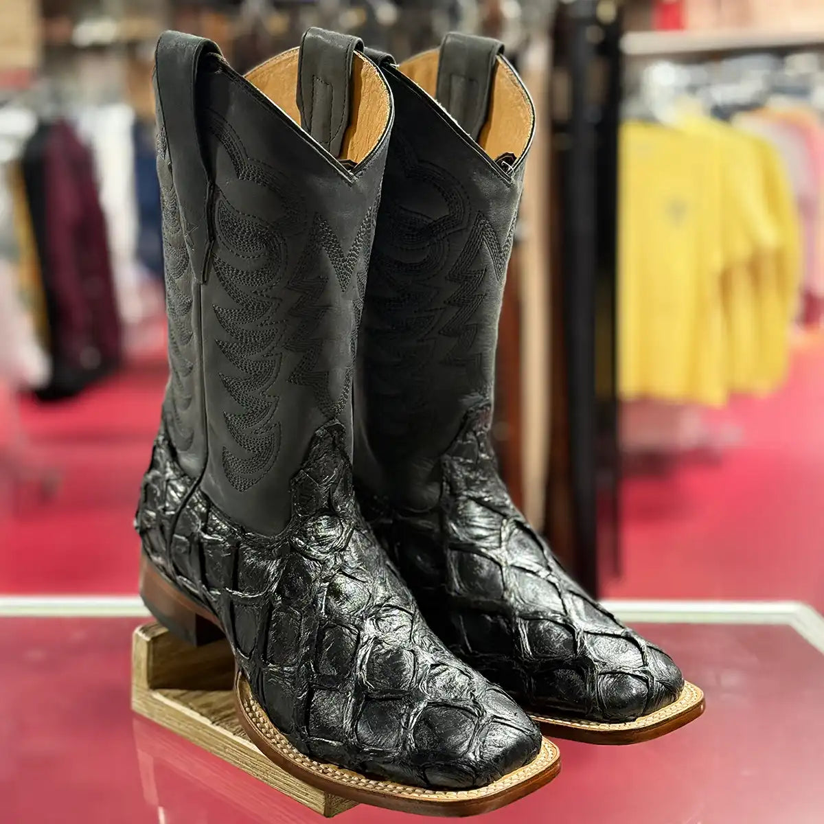 In-store counter display view of the pair of Los Altos men's black glossy pirarucu boots showing the large scale texture and square toe.